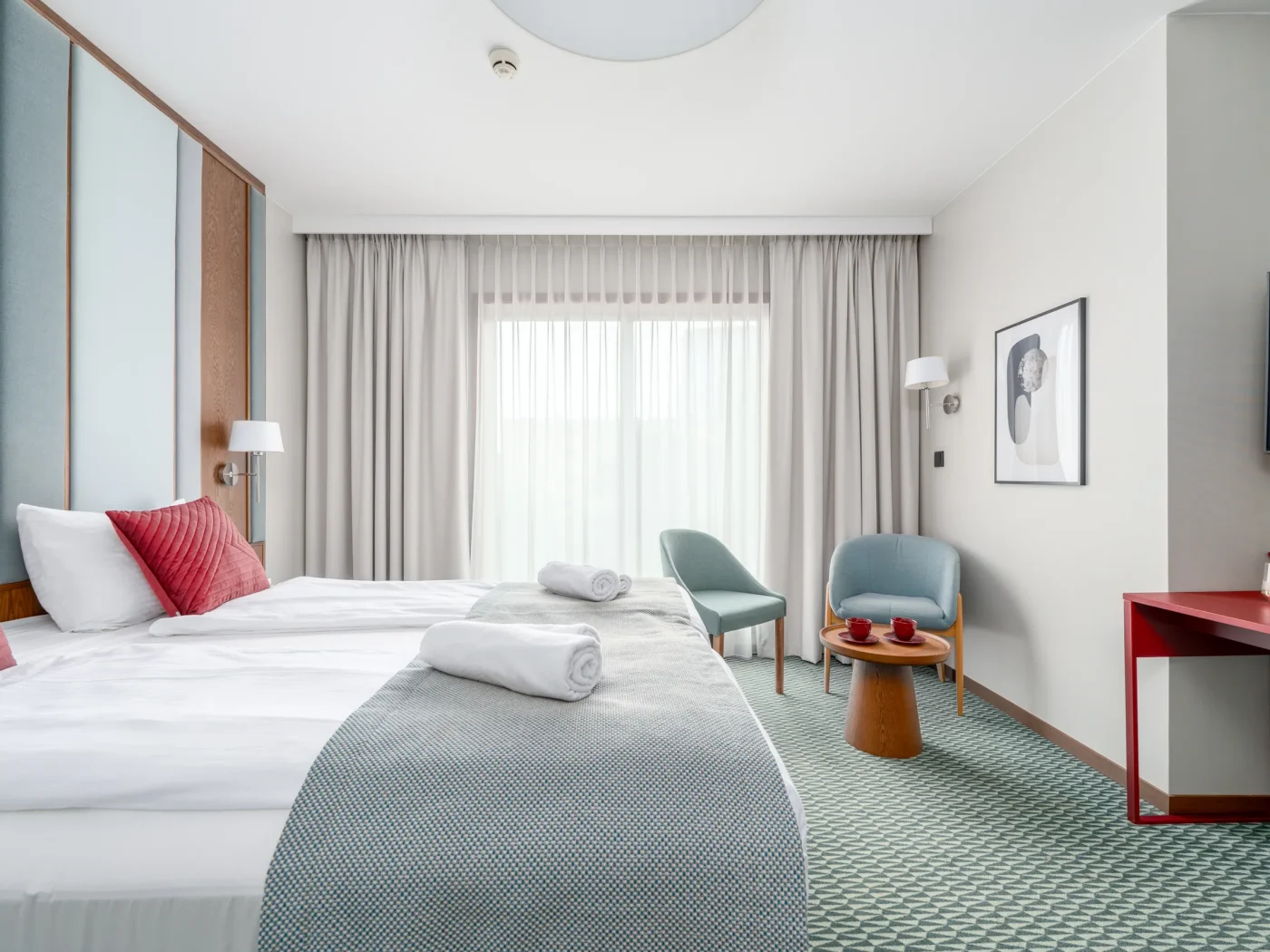 Double bed with a red desk and television in the background