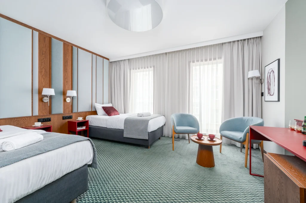 Two beds, armchairs and a window with a sheer curtain