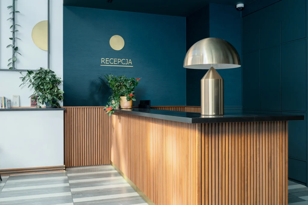 Reception with a wooden counter and brass lamp against a navy-blue wall